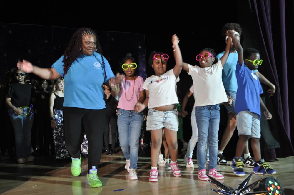 Kids wearing casual clothes and holding hands with staff on stage