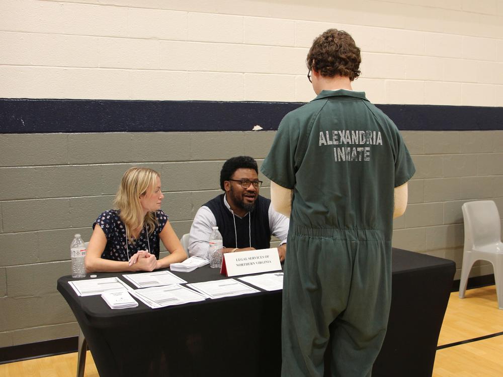 Inmate in green uniform that says Prisoner on the back speaking with two members of Legal Services of Northern VIrginia at the Reentry Resource Fair