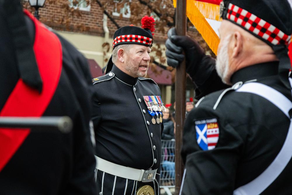 one man in background dressed in formal uniform with badges on his chest, one man blurred in foreground looking the opposite direction