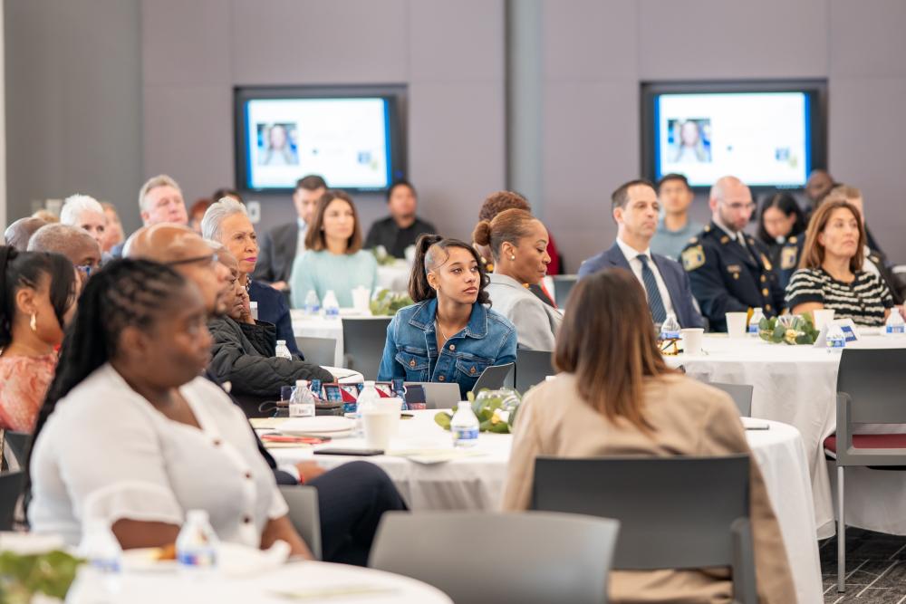Guests seated at round tables watch the program during APD’s inaugural Faith & Blue Prayer Breakfast, with a young attendee in a denim jacket at the center of the image.