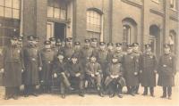 A sepia toned photograph of men in police uniforms in front of a brick building. 