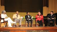 five people seated and talking on a stage