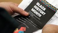 hands holding a paper program featuring graphics and copy for Black History Month
