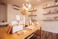 A table in the foreground is decorated with a display of bath items; towels, soaps, and scrubs, and gift boxes arranged decoratively. On the wall behind the table, out of focus, are shelves with more of the same bath and body items displayed artfully in keeping with the store's minimalistic, neutral theme.