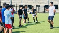 teens in t-shirts and socks on a soccer field listening to a deputy also wearing athletic shoes, shorts and t-shirt