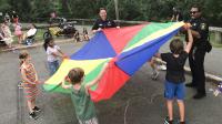 Two deputies and five children playing with a rainbow colored parachute on a playground during National Night Out