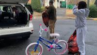 two civilian employees loading a child's bicycle and two large bags full of gifts into a car