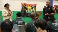 Professional staff member and deputy in blue uniform speak with audience members wearing green jumpsuits before the Black History Month program begins