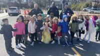 Three deputies in blue uniforms standing with approximately 15 small children in front of them oustide a school