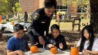 Deputy in a blue uniform helping three children decorate small pumpkins for Halloween