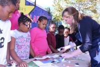 A woman demonstrates an art project to a group of young artists.