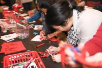 A group of people at a table participate in a craft with paper, scissors, and colored markers. 