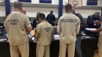 Three inmates in tan jumpsuits seaking with members of a community organization in a gym