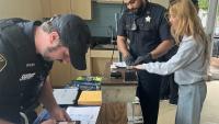 A civilian and two deputies in blue uniforms participating in an expungement clinic, one processing a photo ID and the other fingerprinting the civilian