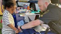 Deputy sheriff in blue uniform taking a digital fingerprint of a small child at a community event