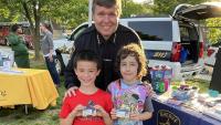 Sheriff in blue uniform with two kids who are holding up photo identification cards and smiling
