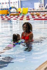 Mother in red swimsuit guiding her daughter in the open swim area of the pool
