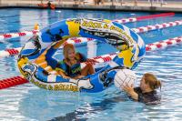 A child sitting inside one blow up pool toy while her mother, who's standing next to her, hands her a blow up volleyball pool toy