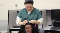 inmate in green uniform braiding the hair of a mannequin head