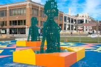 Site See Installation with human figures from torso up in green metal with holes and an orange and yellow square foundation