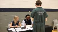 Inmate in green uniform that says Prisoner on the back speaking with two members of Legal Services of Northern VIrginia at the Reentry Resource Fair