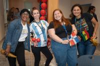 four women, two with flags and one with maracas standing and smiling at camera