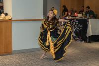 child with black and yellow dress and flower in her hair dancing for a small crowd of people looking on
