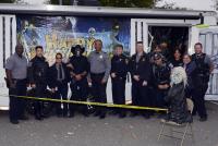 A group of police personnel poses in front of a Halloween backdrop with skeleton decorations and yellow caution tape.