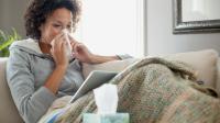 A sick person sitting on a couch with tissues.