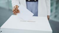 A person puts a paper ballot into a ballot box.