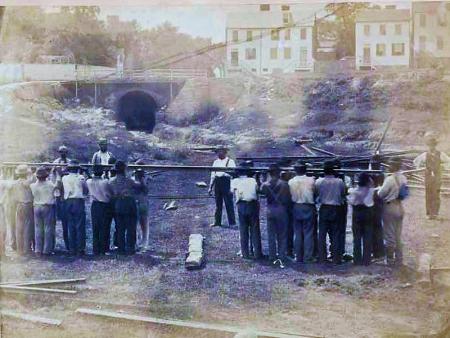 Men holding rail in front of tunnel, damaged black and white photograph