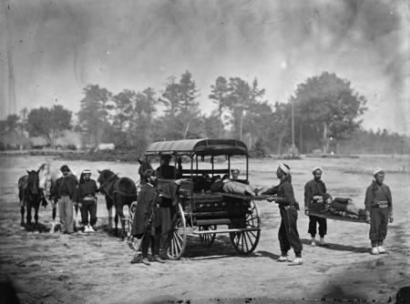 Soldiers putting wounded on stretchers into horse-drawn wagon