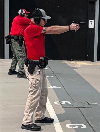 Two firearms instructors, wearing red shirts and BDU style pants, shooting at a range