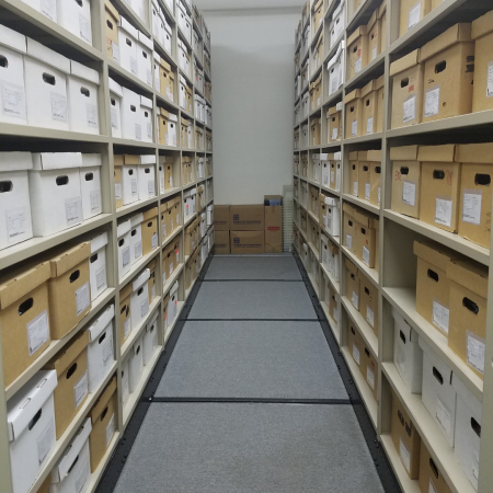 Labeled archival boxes filled with artifacts are stacked on tall shelves in the offsite collections space