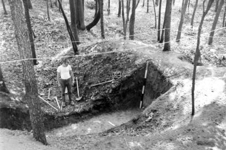 An archaeologist stands beside a partially excavated earthwork at Fort Ward.