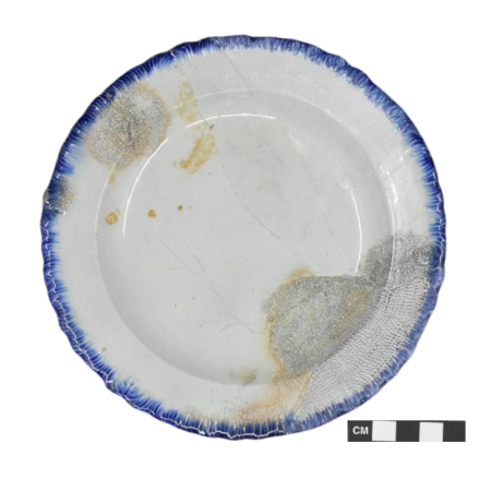 A pearlware plate, approximately 6.5 inches in diameter, with a blue shell-edged design around the outer rim. 