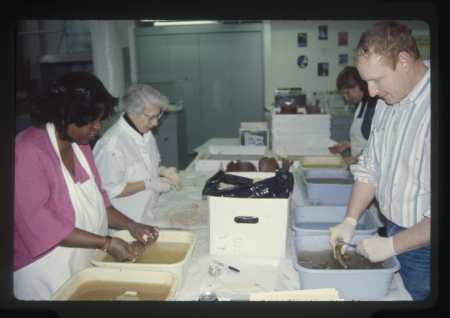 Volunteers wear aprons and gloves while cleaning artifacts with brushes and water in the Alexandria Archaeology lab