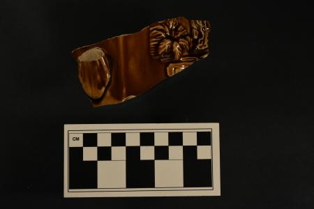 A fragment of a ceramic teapot with a molded brown decoration.