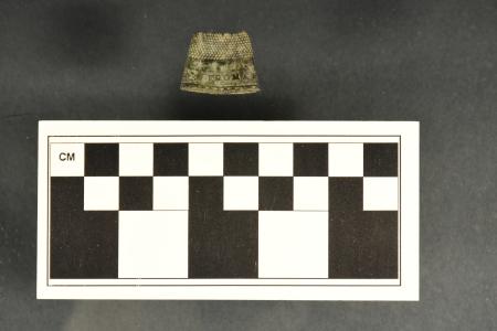 A flattened brass thimble fragment with letters around the base