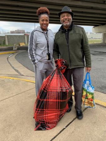 Civilian employee and community member holding a red and black plastic bag full of holiday gifts for kids