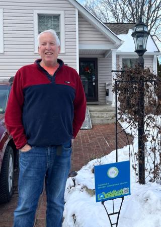 A man stands next to an Eco-City Homes yard sign in front of his house.