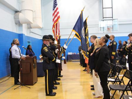 Honor guard of deputies in ceremonial uniforms presenting the colors while audience stands and salutes flag