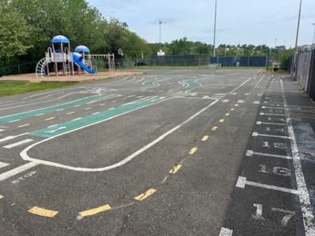 An image of a road network painted on asphalt. A playground and treeline are in the background.