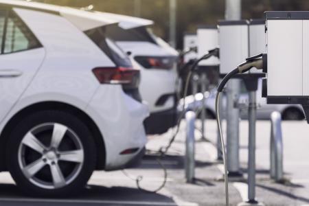 A row of electric vehicle chargers stand in front of parked cars.