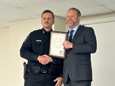 Deputy in a blue uniform receiving a framed award certificate from the criminal justice academy director