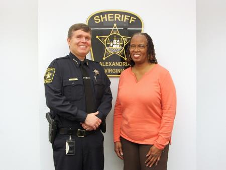 Sheriff and professional employee smiling in front of Alexandria Sheriff's Office sign