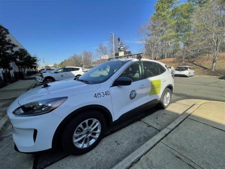 A white car with a City of Alexandria seal, sensor equipment, and a decal that says "Road Survey in Progress"