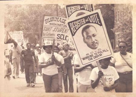 Protesters marching with signs, including ones with photos of Martin Luther King, Jr. and the words "Register to Vote."