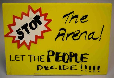 A handmade yellow poster reads, “Stop the Arena! Let the People Decide!!!!!”