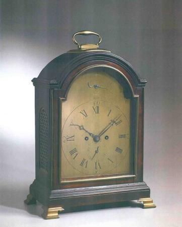 A bracket clock, with a wooden case and brass handle and feet, is stopped at 10:09.